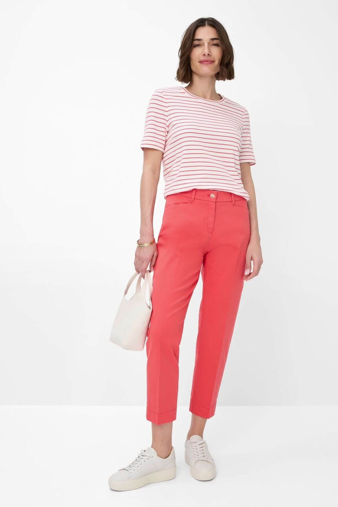 Femme portant un t-shirt rayé CIRA blanc et rouge avec un pantalon corail, style moderne et décontracté.