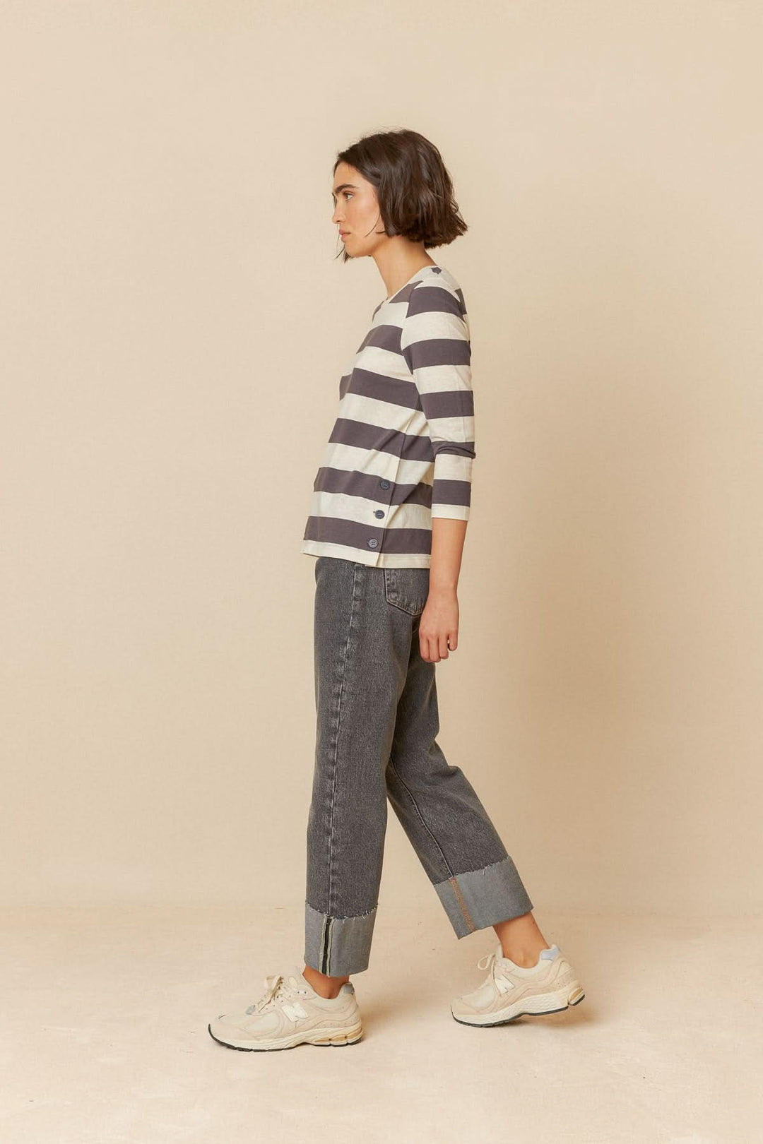 Femme portant un t-shirt rayé à manches 3/4 et un pantalon gris, dans un style décontracté.