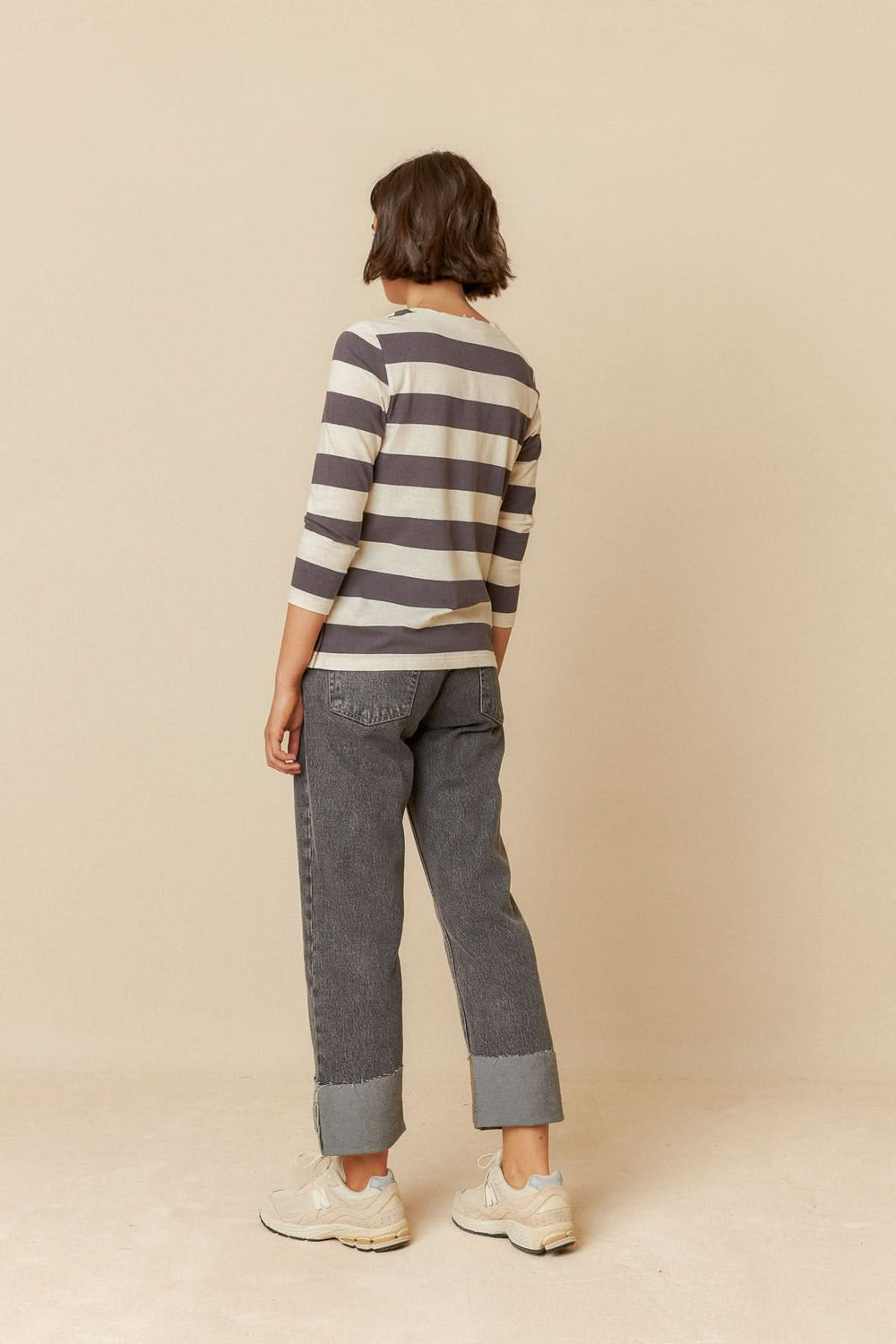 Femme vue de dos portant un T-shirt rayé à manches 3/4 et un pantalon gris, style décontracté.