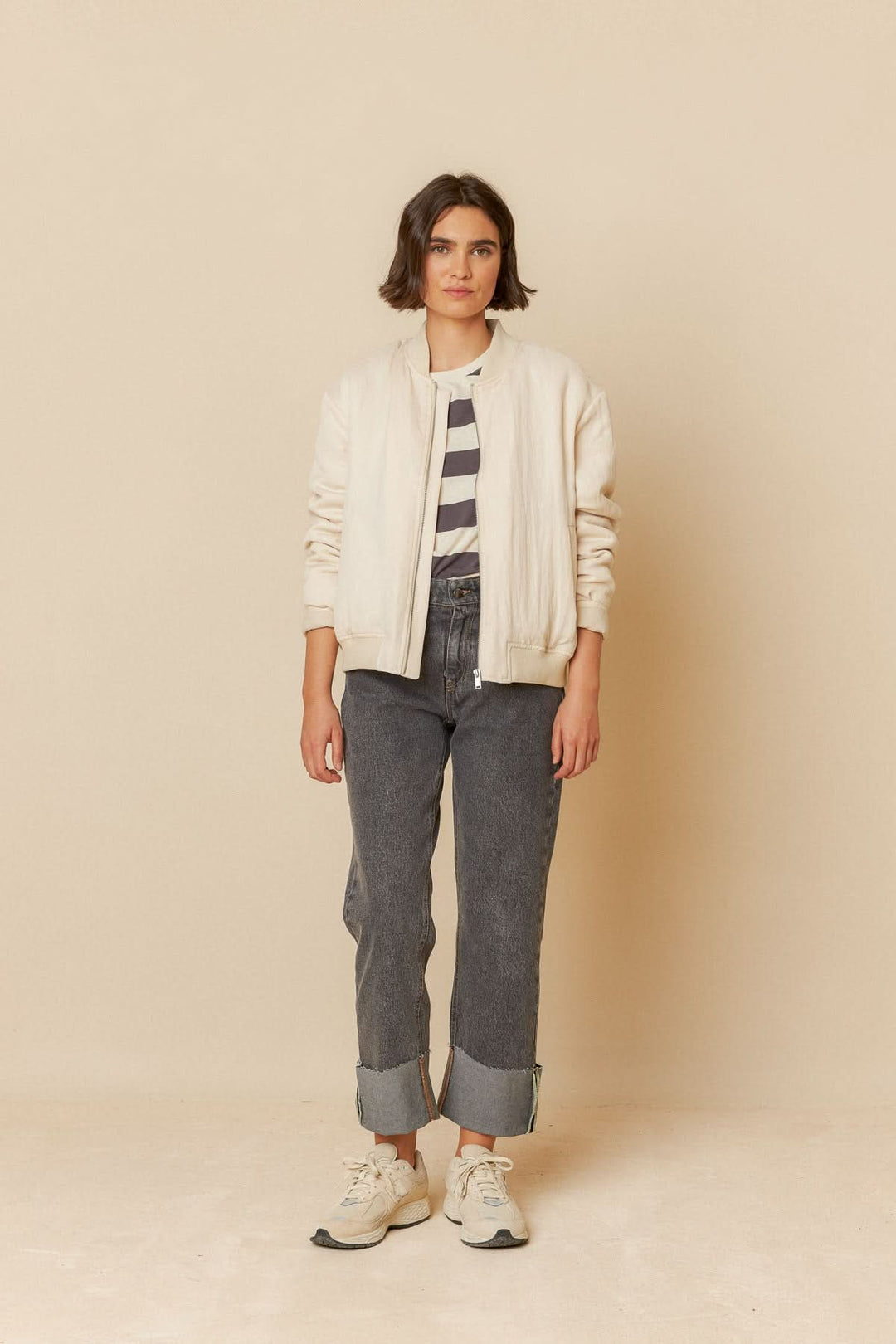 Femme portant un t-shirt rayé à manches 3/4, bomber beige et jeans, sur fond neutre.