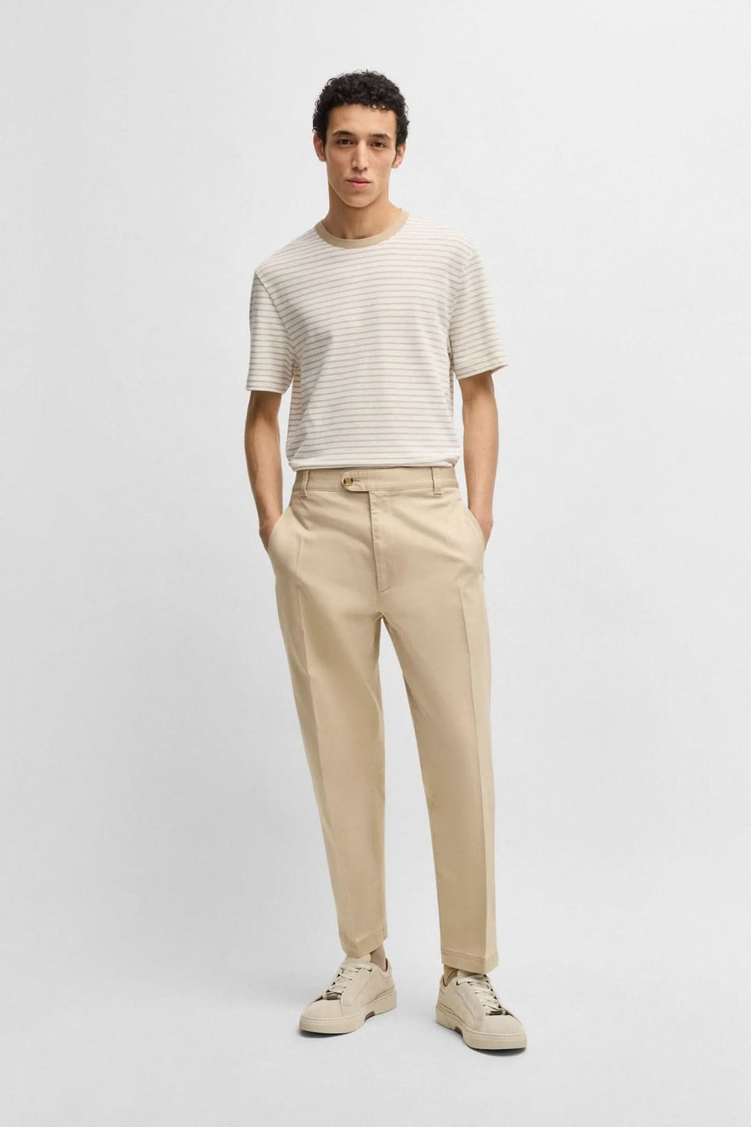Homme portant un t-shirt rayé et un pantalon beige, look moderne et décontracté.