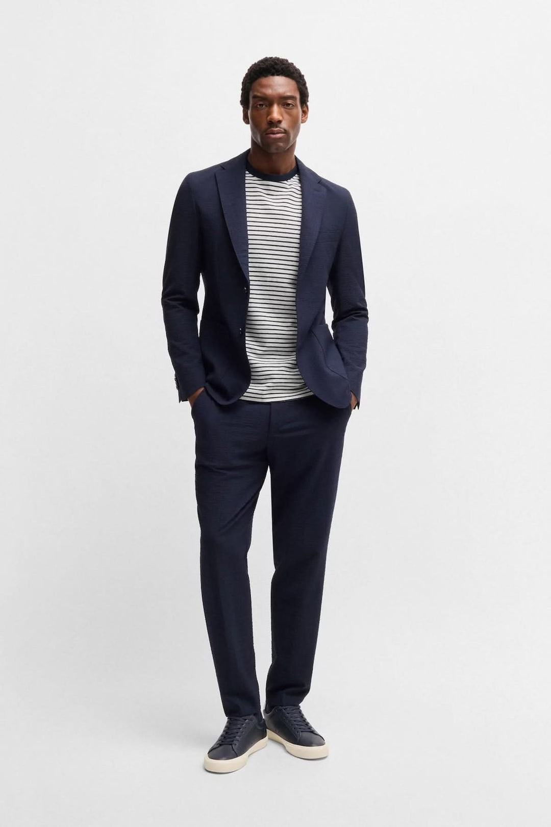 Homme en costume navy avec t-shirt rayé, look moderne et décontracté.