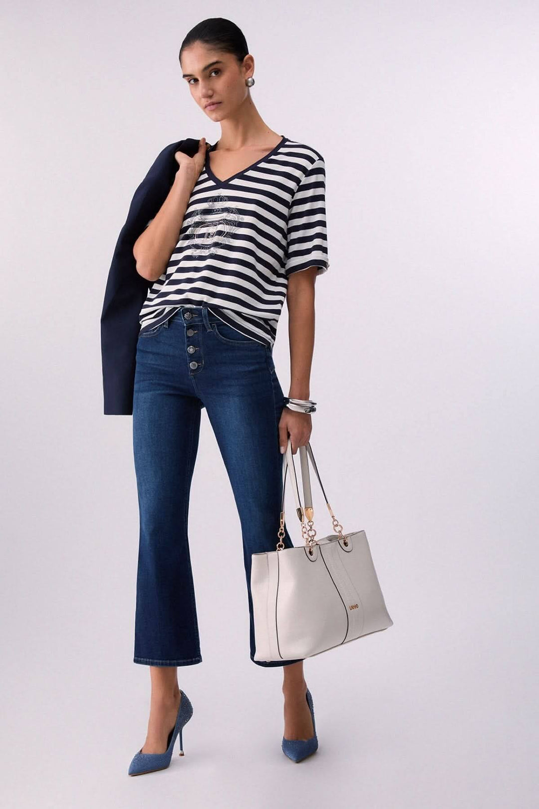 Femme portant un t-shirt rayé col en V avec motif décoratif, associé à un jean et un sac à main.