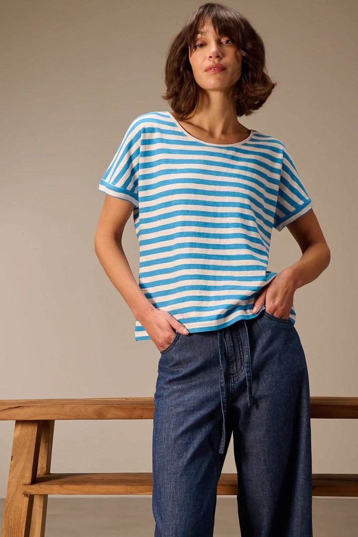 Femme portant un t-shirt rayé à manches courtes coupe décontractée, motif bleu et blanc, avec encolure ronde et épaules tombantes.