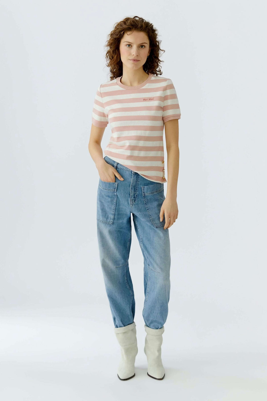 Femme portant un T-shirt à rayures avec un jean et des bottes blanches, style moderne et élégant.