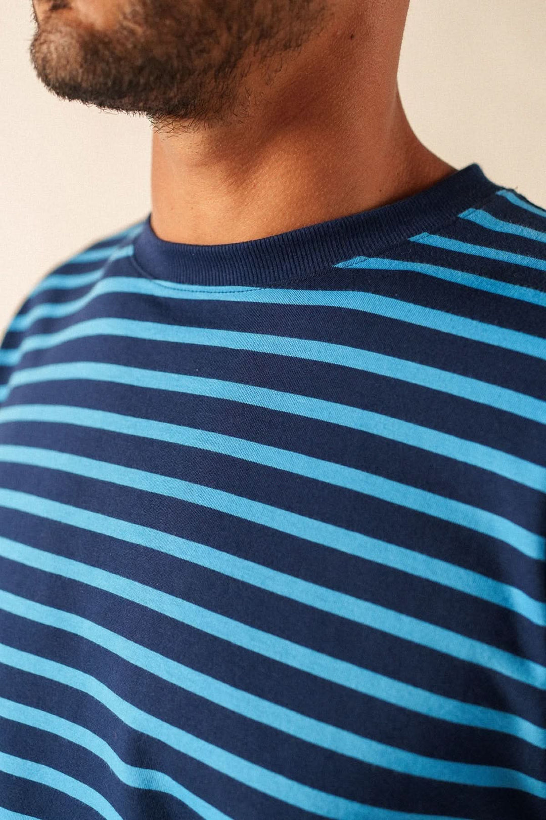Homme portant un T-shirt à rayures classique bleu et noir, coupe régulière avec encolure arrondie et manches courtes. Décris moi le produit.