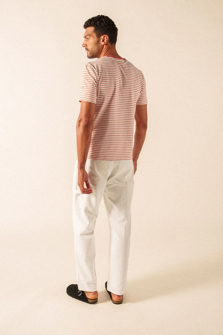 Homme portant un T-shirt à rayures fines et pantalon blanc, style décontracté et moderne.