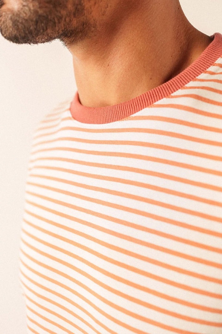 Homme portant un T-shirt à rayures fines avec encolure arrondie, manches courtes, en tissu doux. Style décontracté et soigné.