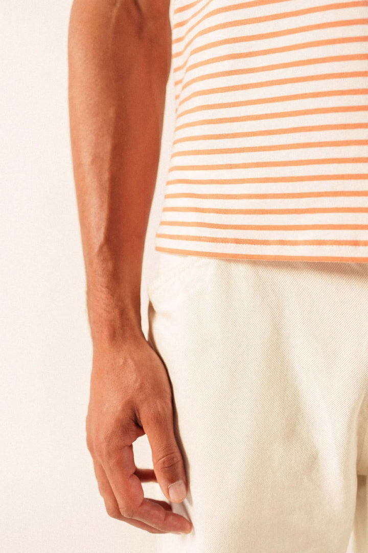 Homme portant un T-shirt à rayures fines orange et blanc, manches courtes, avec un pantalon clair, silhouette décontractée et moderne.