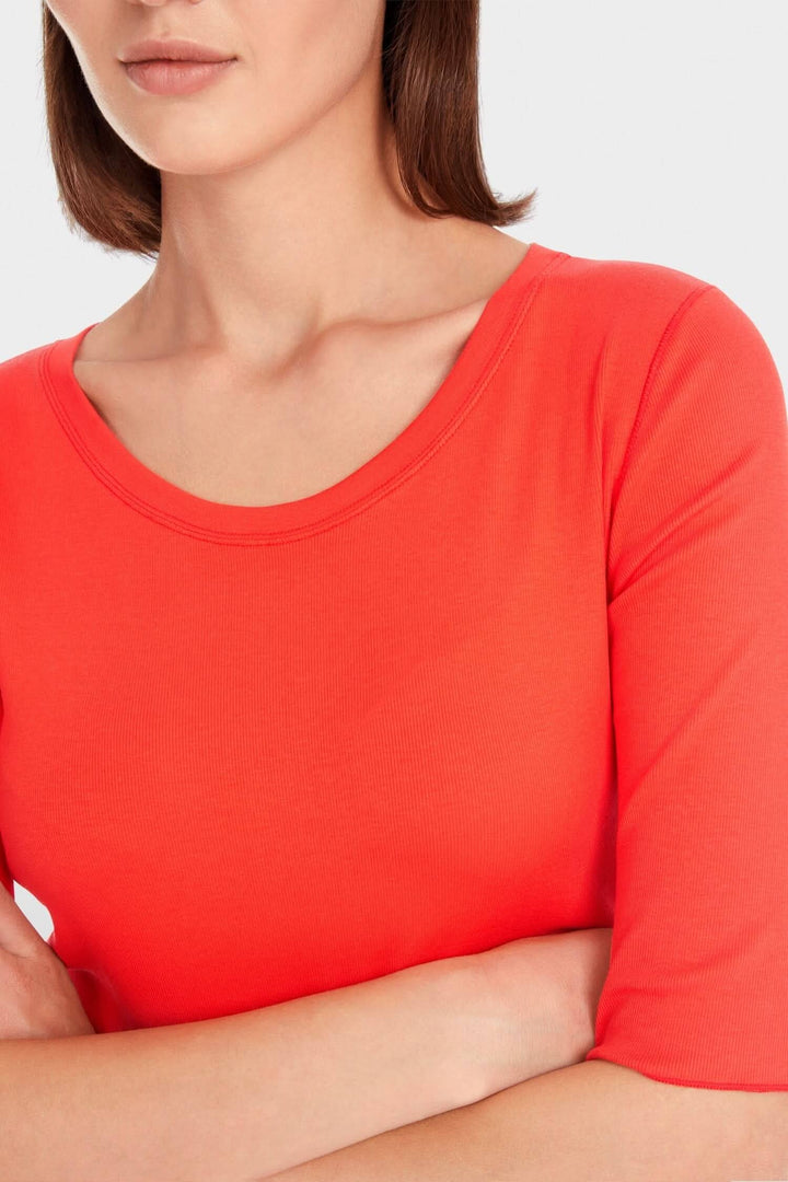 Close-up of a woman wearing a fitted coral T-shirt with a round neckline and 3/4 sleeves.