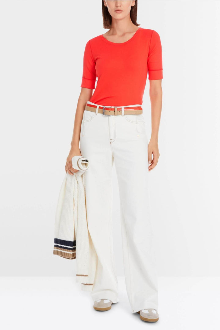 Femme portant un t-shirt rouge à manches courtes et un pantalon blanc, accessoirisé d'une ceinture.