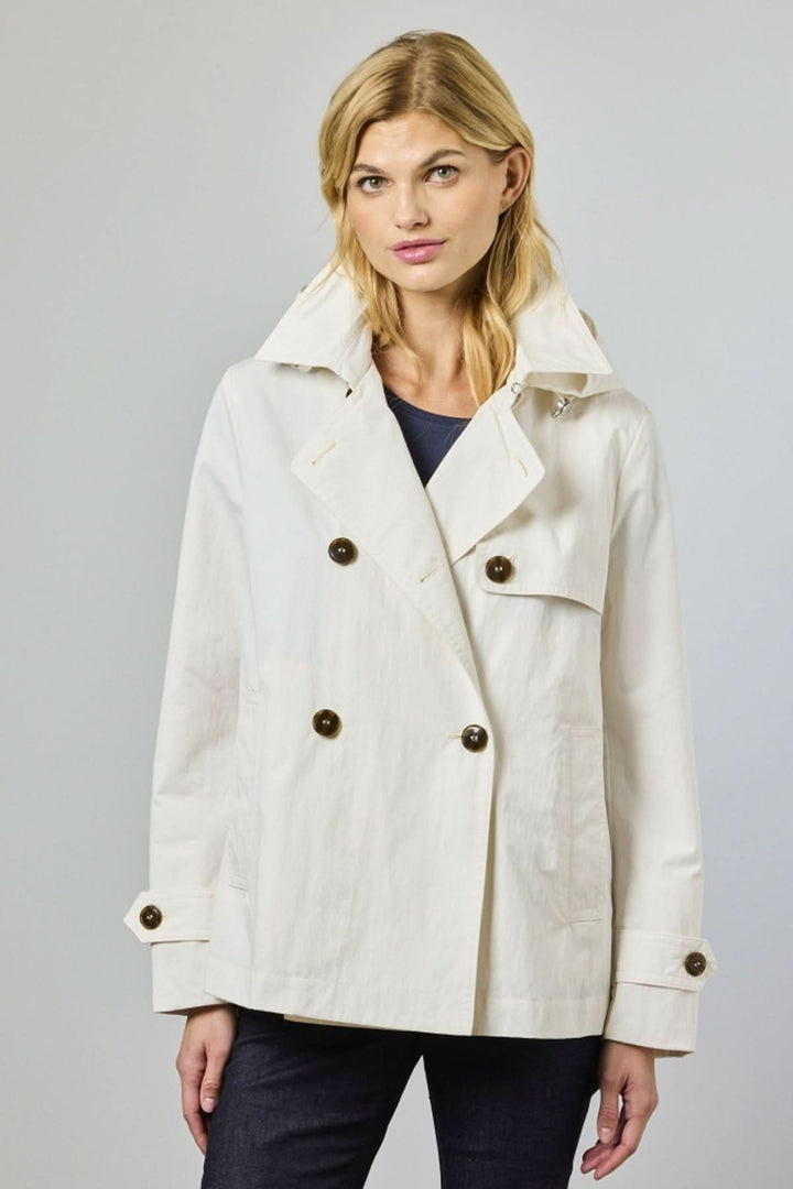 Femme portant un trench court croisé blanc, à coupe droite et col large, boutons contrastants, style moderne et épuré.