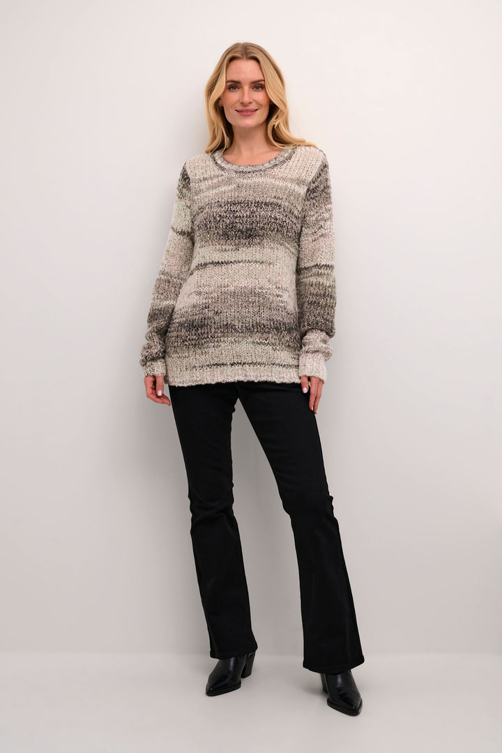 Femme portant un tricot au mélange de couleurs avec pantalon noir et bottines, look moderne et décontracté.