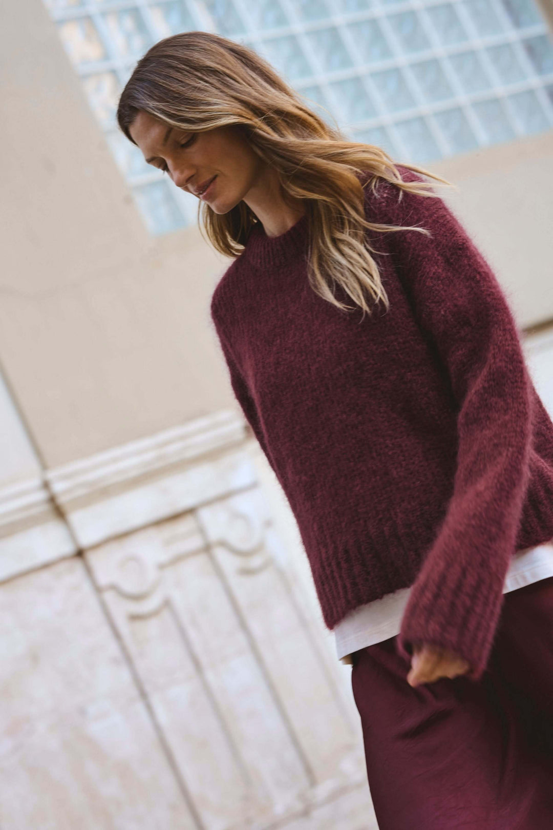 Femme portant un tricot ample col rond bordeaux, style moderne avec jupe, parfait pour la saison froide.
