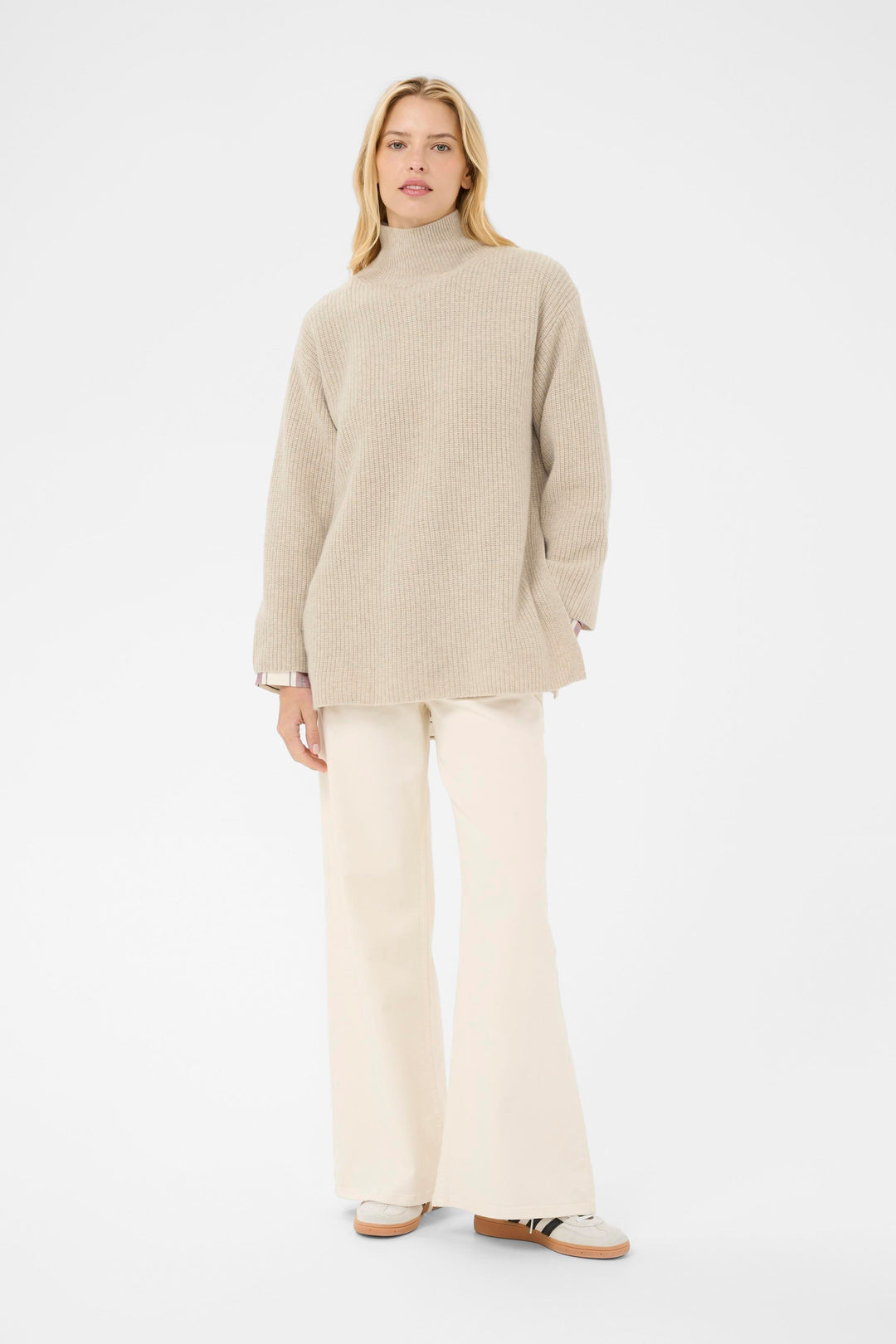 Femme portant le tricot Sofiya à col montant, coupe ample et droite, style moderne avec pantalon évasé, idéal pour temps frais.