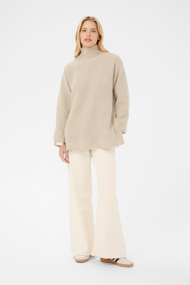 Femme portant le tricot Sofiya à col montant, coupe ample et droite, style moderne avec pantalon évasé, idéal pour temps frais.