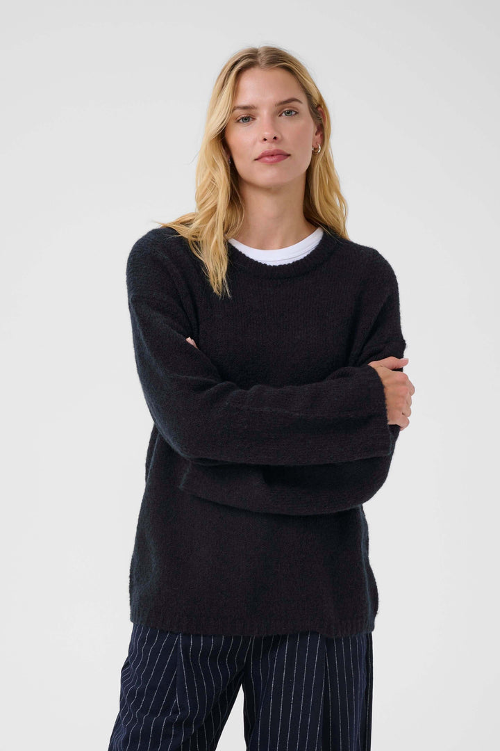 Femme portant un Tricot Spence noir, col rond et manches longues, parfait pour un look décontracté chic.