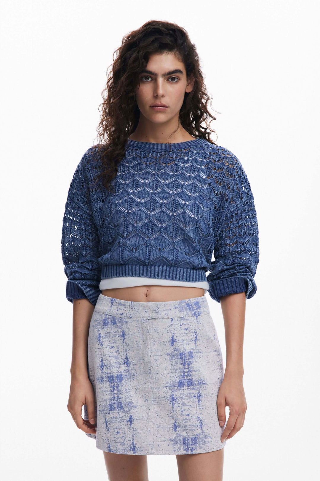 Tricot ajouré bleu, court et ample, avec manches longues, porté sur une jupe tendance.