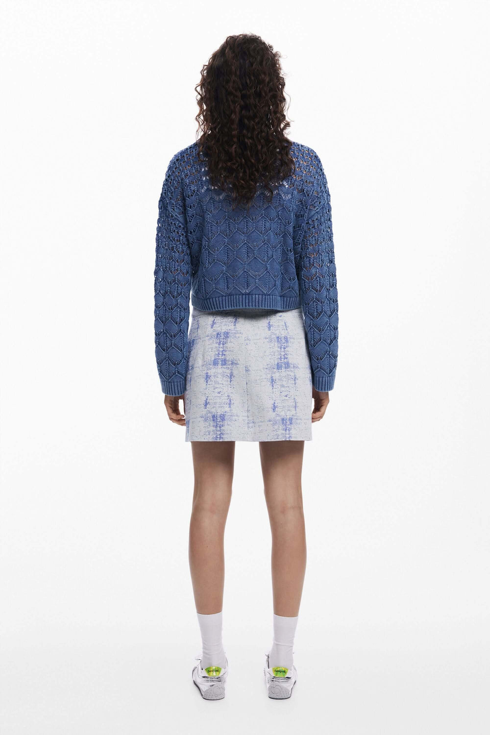 Femme portant un tricot ajouré bleu avec une jupe en denim, vue de dos.