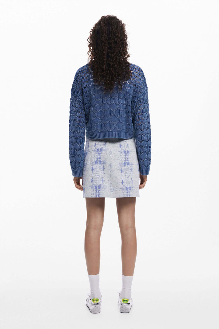Femme portant un tricot ajouré bleu avec une jupe en denim, vue de dos.