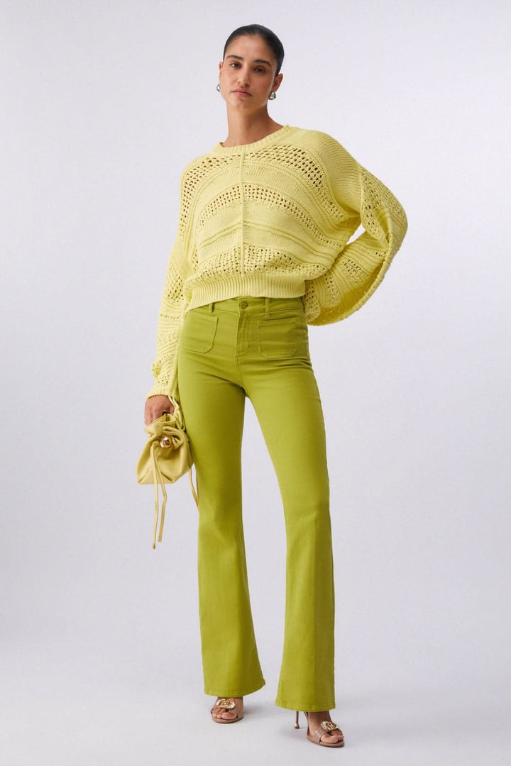 Femme portant un tricot ajouré à manches longues avec un pantalon vert citron, ajout contemporain et féminin aux tenues.