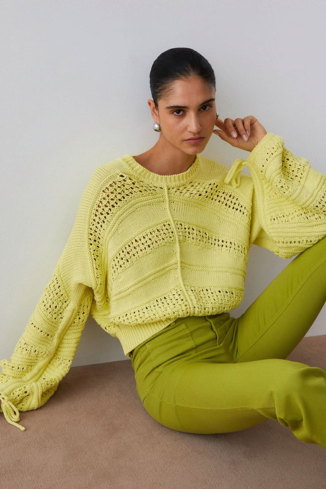 Tricot ajouré à manches longues en maille jaune porté par une femme assise, style moderne et féminin pour la mi-saison.