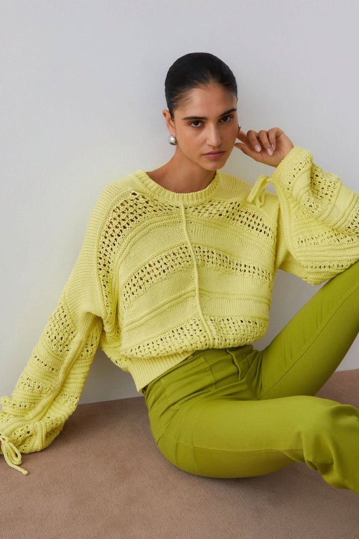 Tricot ajouré à manches longues en maille jaune porté par une femme assise, style moderne et féminin pour la mi-saison.