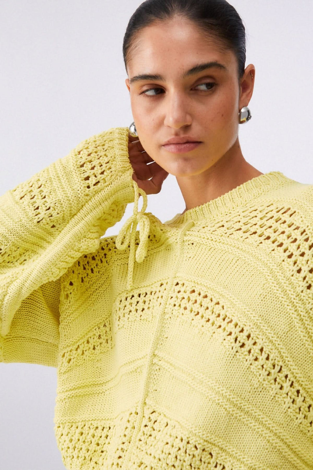 Femme portant un tricot ajouré à manches longues jaune avec motif raffiné et maille texturée, ajoutant une touche contemporaine.
