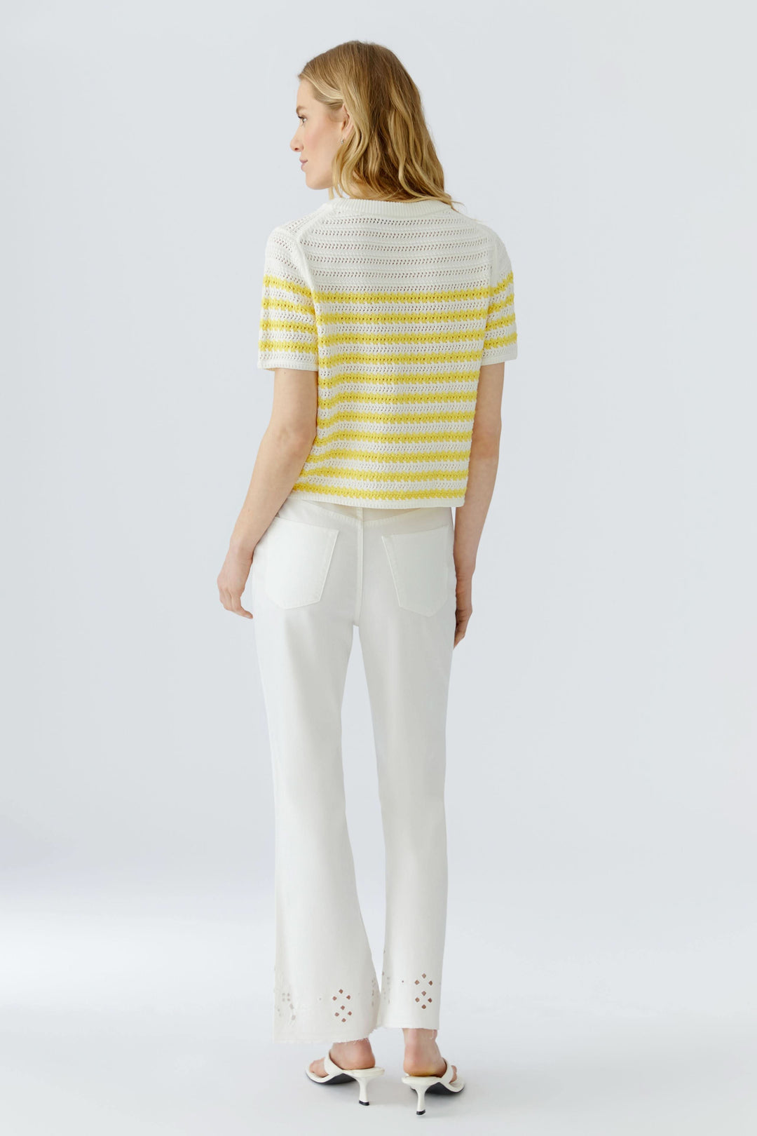 Femme portant un Tricot ajouré à rayures manches courtes en jaune et blanc, vu de dos, avec pantalon blanc.