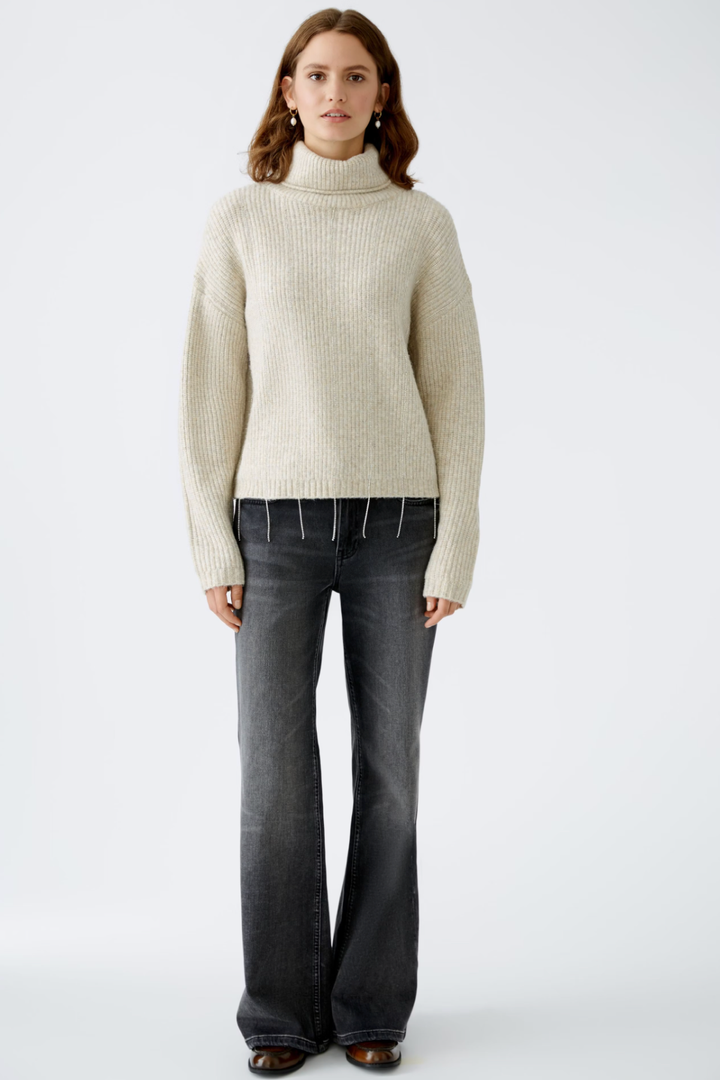 Tricot avec col roulé et maille côtelée, associé à un jean noir évasé, style décontracté et moderne.