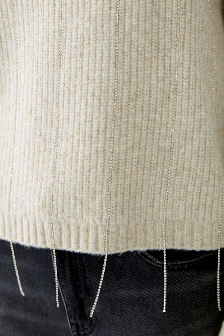 Tricot beige côtelé avec fils pailletés et broderies scintillantes, détail de l'ourlet.