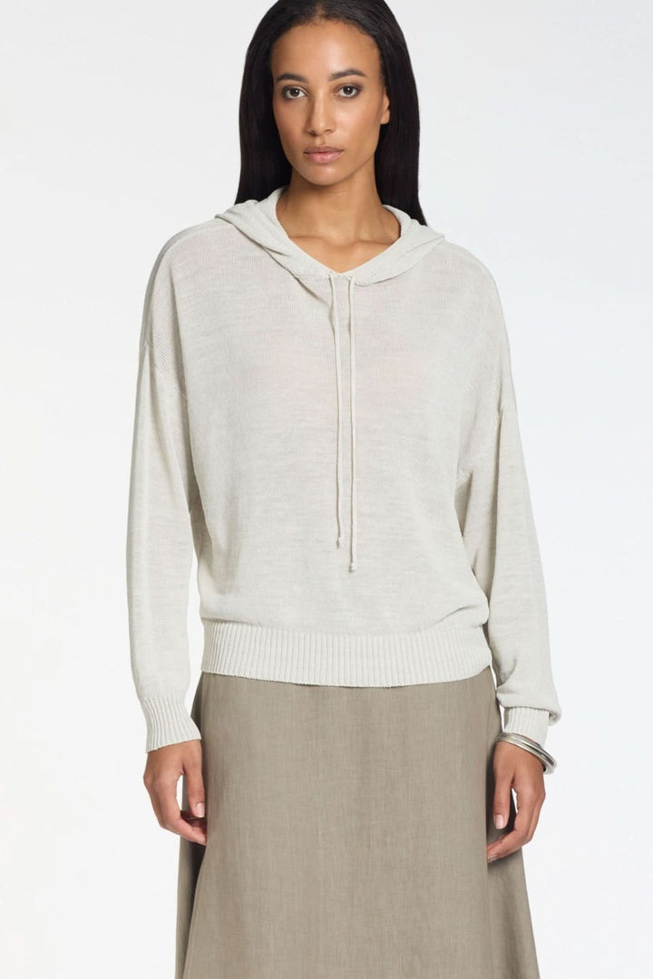 Femme portant un tricot à capuche en maille légère avec manches longues et finitions côtelées, adapté pour un look décontracté.