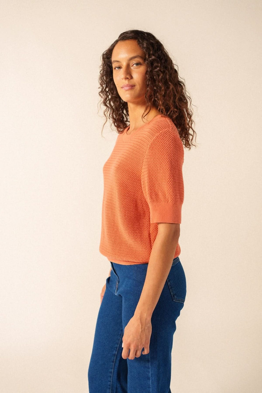 Femme portant un Tricot manches courtes PROVENCE en maille texturée orangée, coupe droite, avec un jean bleu.