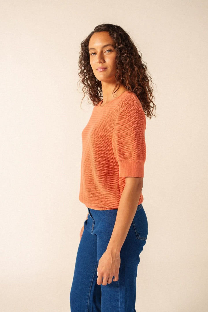 Femme portant un Tricot manches courtes PROVENCE en maille texturée orangée, coupe droite, avec un jean bleu.