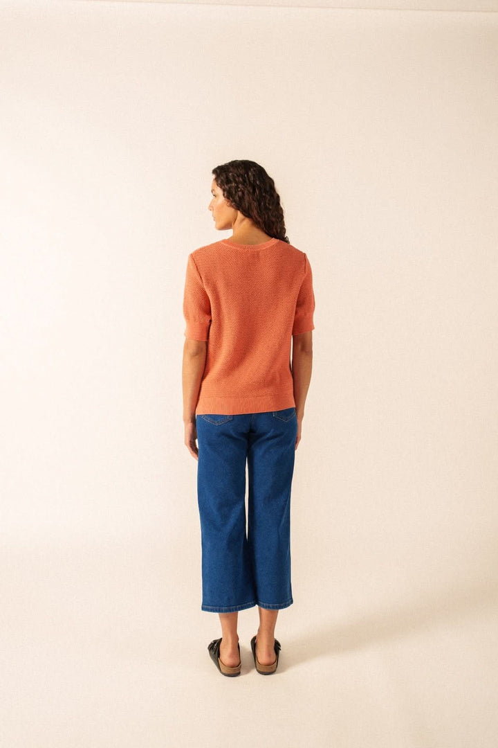 Femme portant un Tricot manches courtes PROVENCE texturé, coupe droite, couleur orange, avec jean bleu, vue arrière élégante.