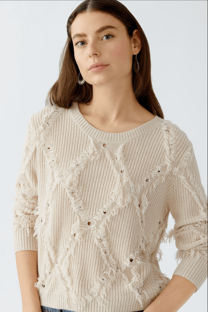 Tricot au motif losange avec franges, col ras du cou, coupe décontractée et détails métalliques.