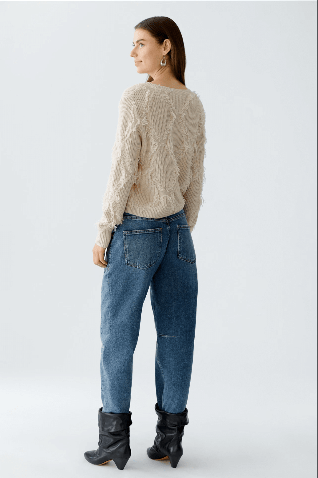 Femme portant un tricot à motif losange beige, vu de dos, associé à un jean décontracté et des bottes noires.