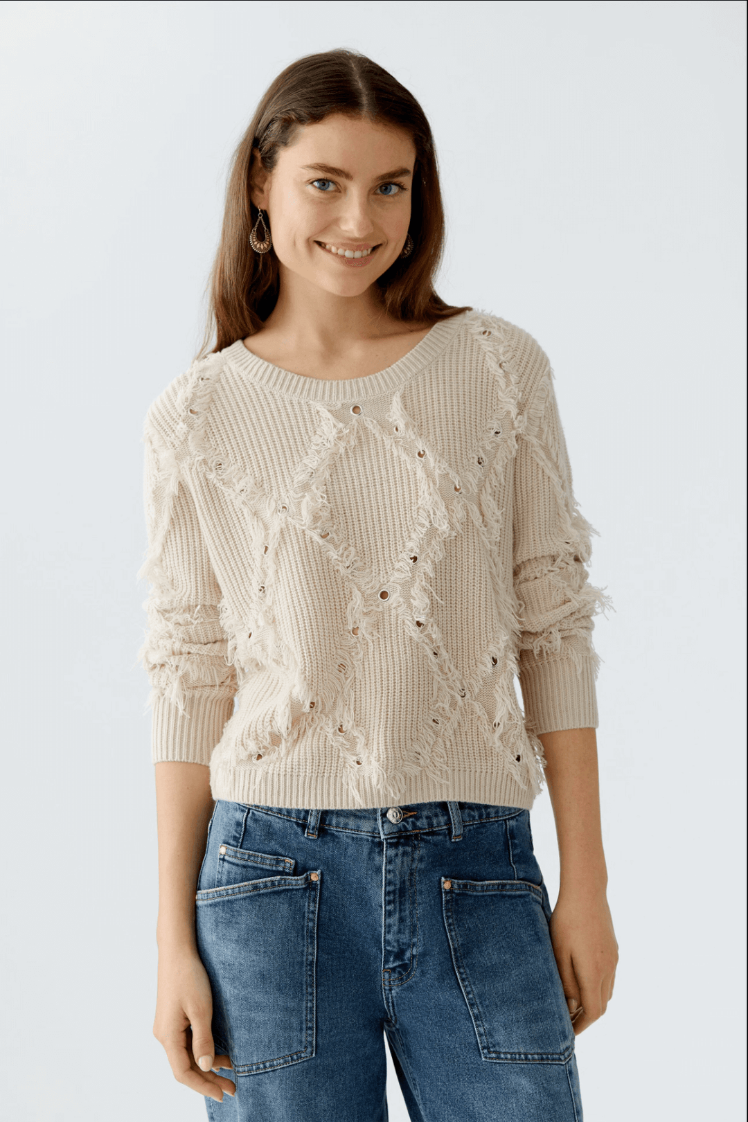 Tricot court motif losange beige avec franges et détails métalliques, porté avec un jean.