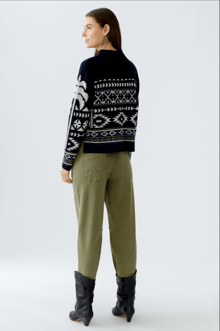 Femme portant un tricot à motif norvégien, coupe courte, avec pantalon décontracté et bottes noirs.