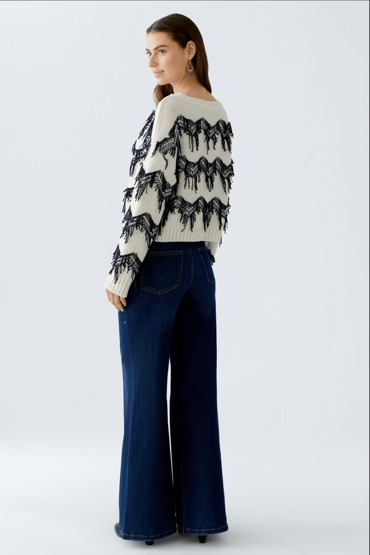 Tricot motif zigzag avec franges tricotées et coupe carrée, porté avec un jean évasé.