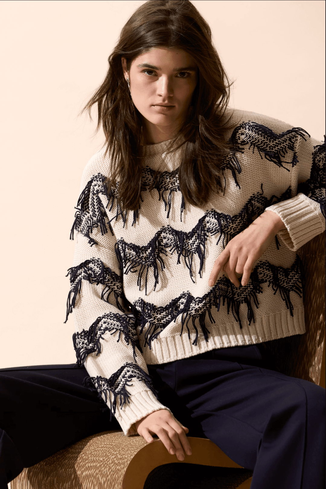 Pull tricot zigzag à franges texturées, coupe carrée et encolure sous-marine, porté avec un pantalon.