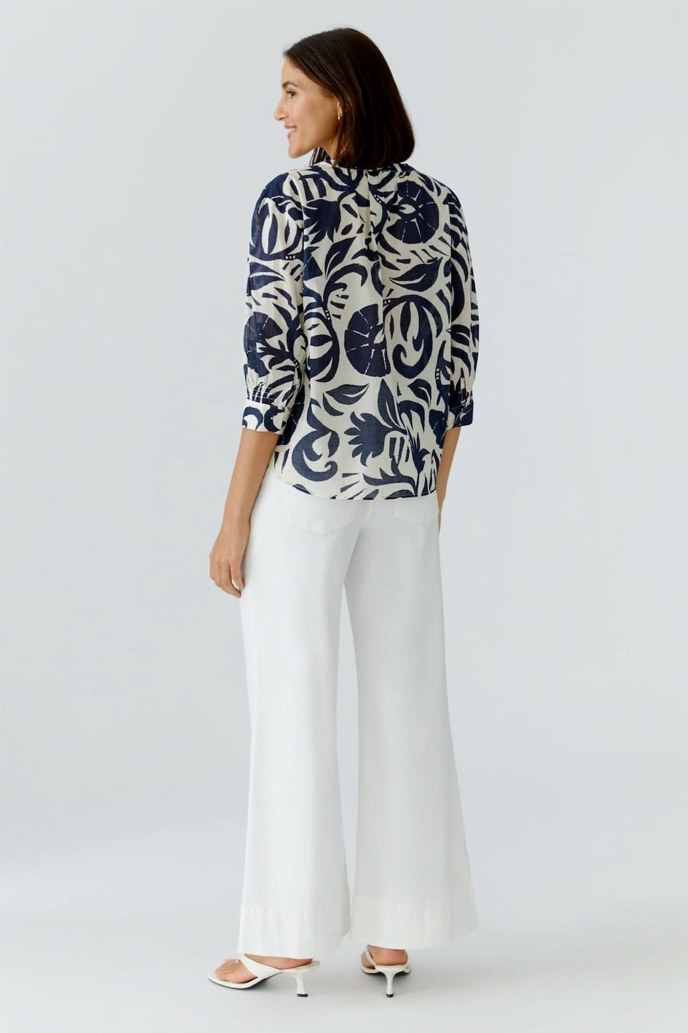 Femme portant une tunique fluide à imprimé graphique avec pantalon blanc, vue arrière. Tunique élégante et confortable.