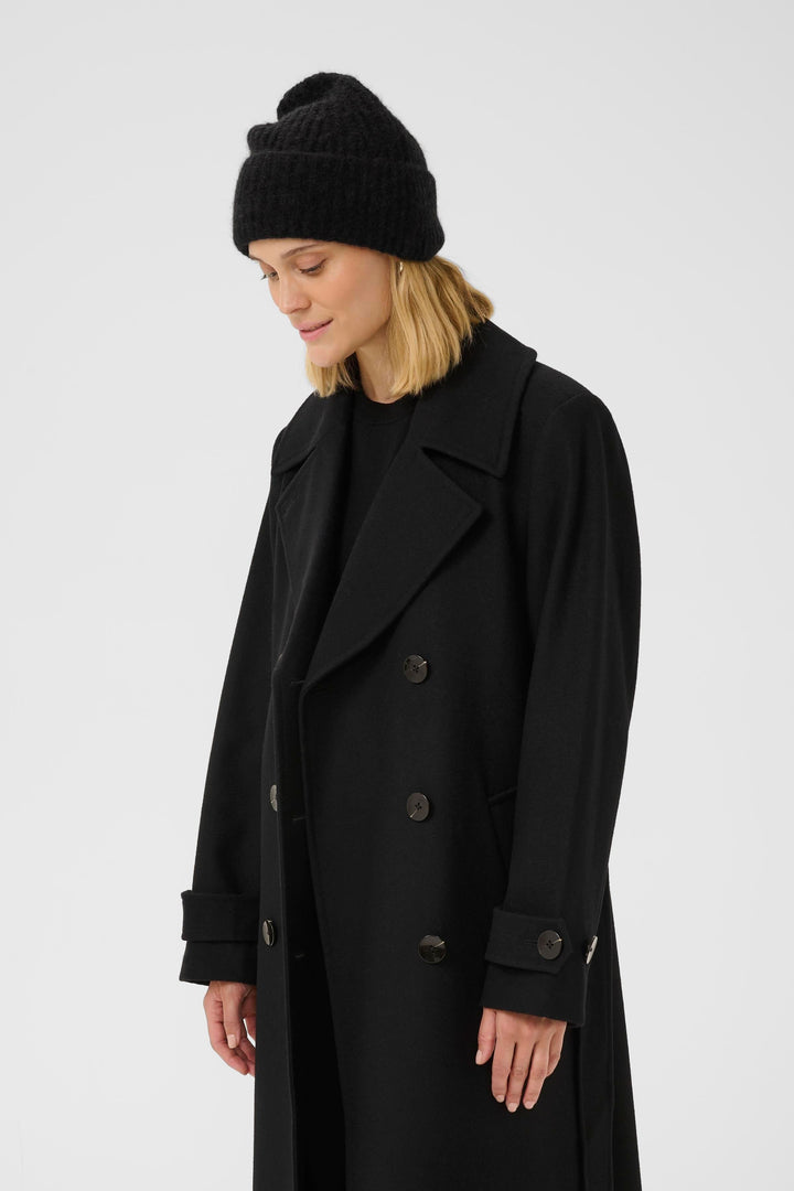 Person wearing a black ribbed knit tufted tuque and black coat, showcasing a modern casual winter style.