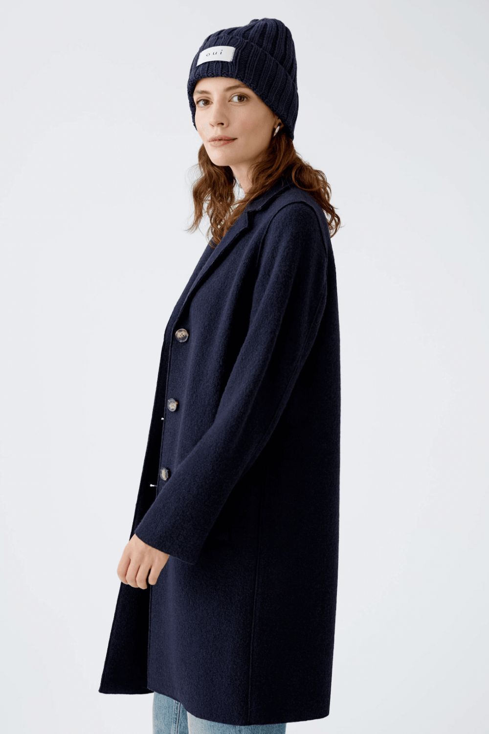 Femme portant une tuque en tricot bleu marine et un manteau oversize élégant pour un look urbain chic.