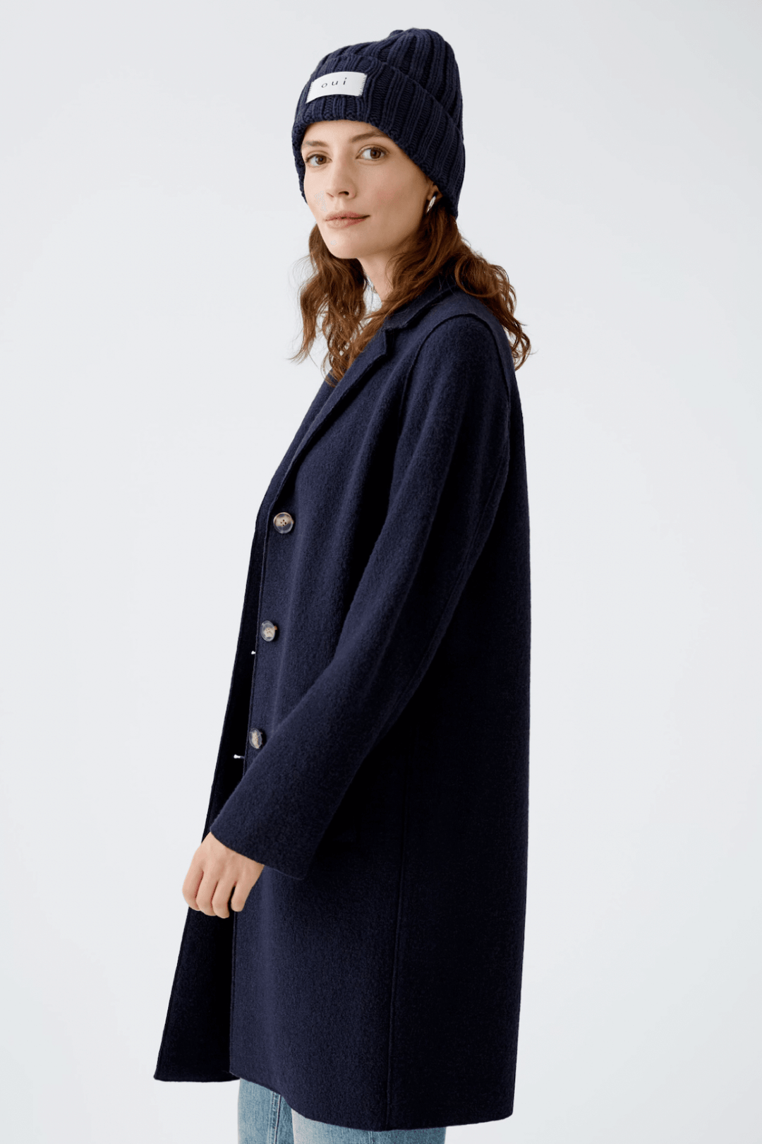 Femme portant une tuque en tricot bleu marine et un manteau oversize élégant pour un look urbain chic.