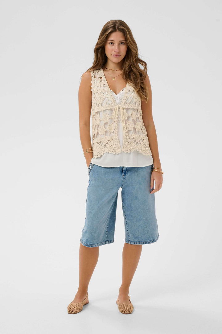 Femme portant Veste Lotu sans manches en crochet avec motif floral texturé, style bohème élégant, sur une blouse blanche.