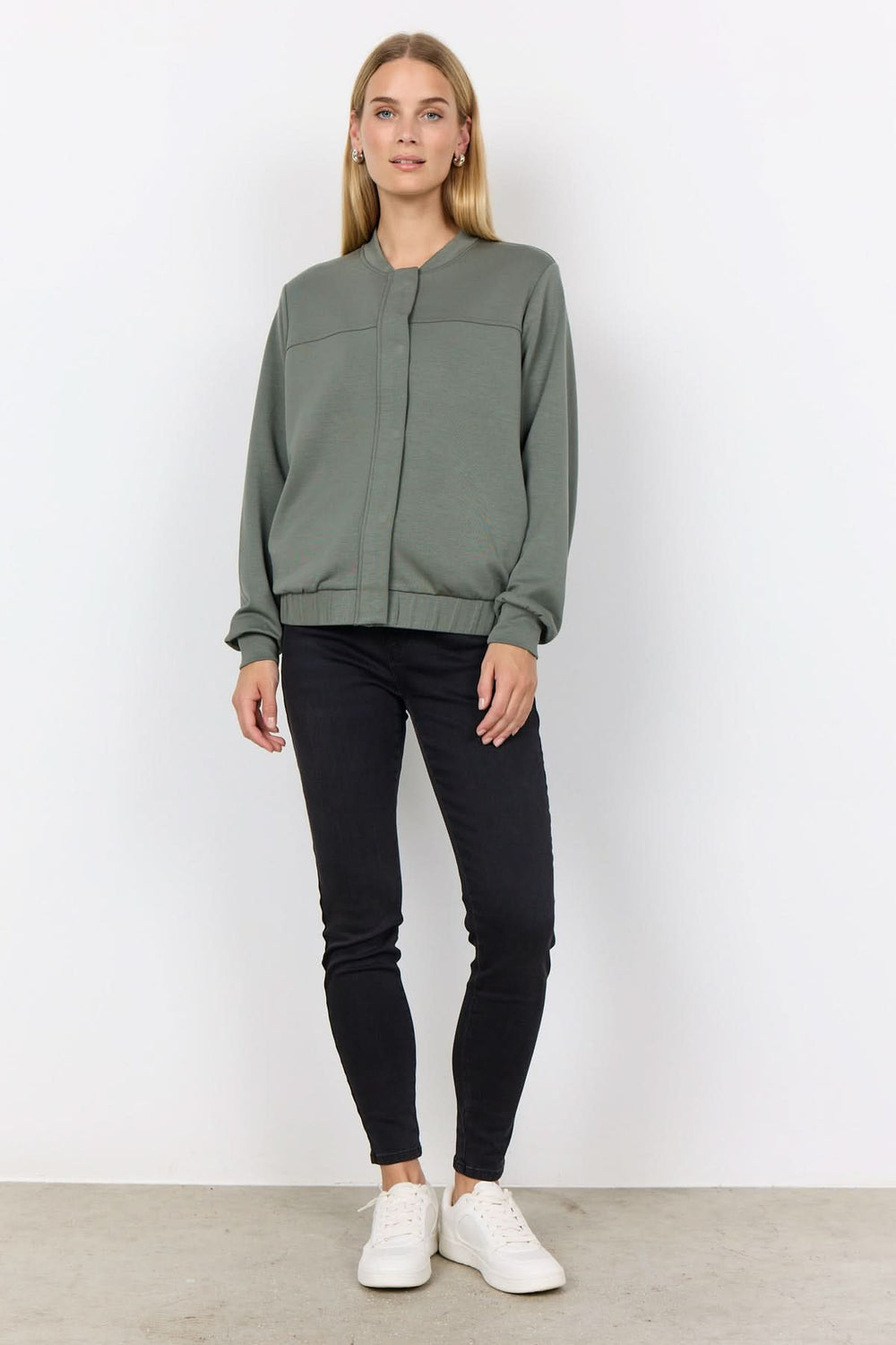 Veste à bouton-pression verte portée avec un pantalon noir et des baskets blanches, affichant un style chic et décontracté.