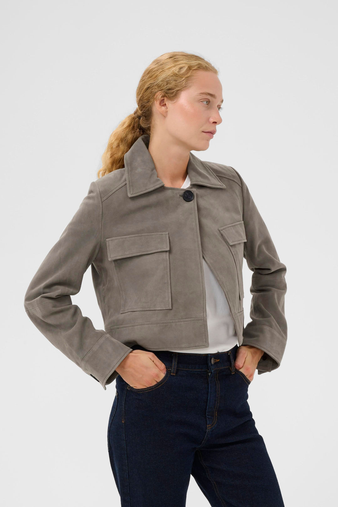 Veste courte Carnika en suédé avec silhouette structurée et coupe élégante, portée par un mannequin, style utilitaire chic.