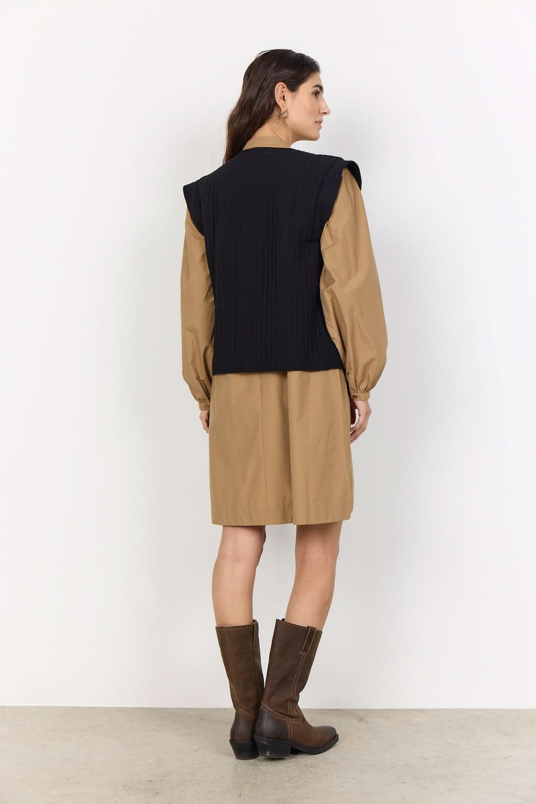 Femme portant une veste courte sans manches noire, encolure ronde, coupe régulière, ouverte, broderies florales, style décontracté.