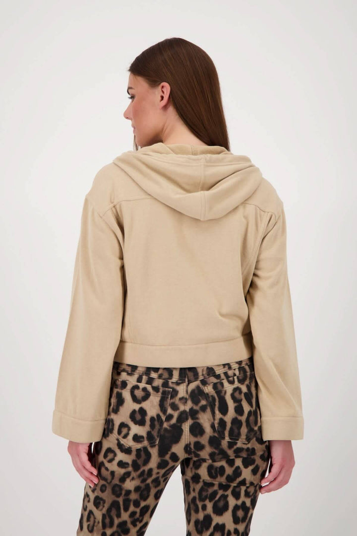 Femme portant une veste courte à capuchon beige, vue de dos, avec un pantalon à imprimé léopard.